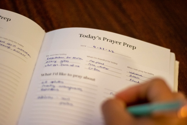 Puede incluir: Una libreta blanca con las palabras "Today's Prayer Prep" escritas en la parte superior. La fecha "4-23-22" est&aacute; escrita debajo del t&iacute;tulo. La libreta est&aacute; dividida en secciones para "Mis preocupaciones de hoy", "Por lo que estoy agradecido hoy", "Sobre lo que me gustar&iacute;a orar" y "Por qui&eacute;n puedo orar hoy".
