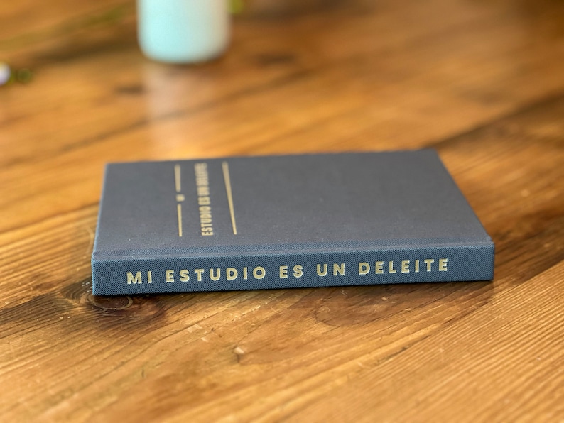 May include: A dark blue notebook with the text "MI ESTUDIO ES UN DELEITE" in gold lettering on the spine.