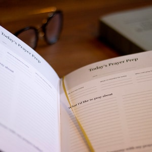 Puede incluir: Un diario abierto con p&aacute;ginas rayadas para escribir oraciones. Las p&aacute;ginas est&aacute;n etiquetadas como "Preparaci&oacute;n de la oraci&oacute;n de hoy" e incluyen secciones para "Por lo que estoy agradecido hoy", "Por lo que puedo orar hoy" y "Sobre lo que me gustar&iacute;a orar".
