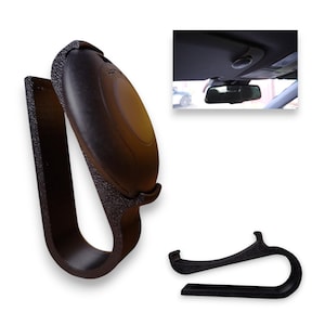 May include: Black car visor clip with a textured finish, designed to hold a garage door opener. The clip has a curved design and a secure grip. An additional clip is also shown. The image also includes a view of the car's interior.