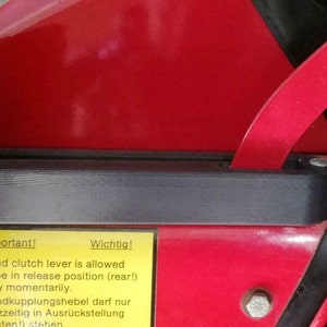 Peut inclure: Un panneau d'avertissement jaune avec du texte noir en anglais et en allemand. Le panneau indique "Important! Hand clutch lever is allowed to be in release position (rear!) only momentarily. Wichtig! Handkupplungshebel darf nur kurzzeitig in Ausrückstellung (hinten!) stehen."