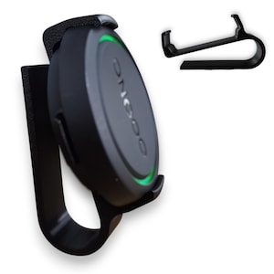 May include: A black device with the word "ONGOO" printed on it, featuring a green light and a clip. The device is attached to a black holder. A separate black clip is also visible.