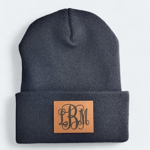 May include: A navy blue beanie with a brown leather patch featuring the monogram "LBM" in a script font.