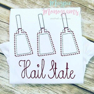 May include: White t-shirt with three maroon cowbells and the text "Hail State" in maroon embroidery.