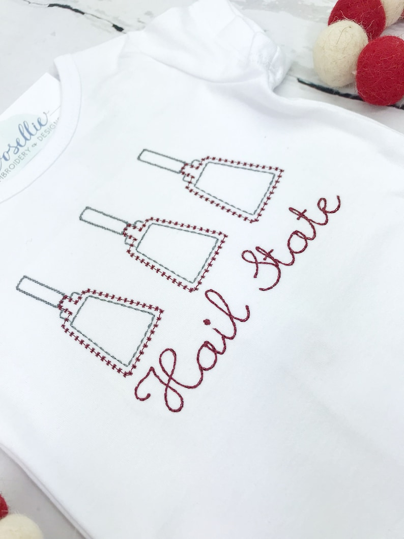 May include: White baby onesie with three gray jingle bells and the text "Hail State" embroidered in maroon thread.