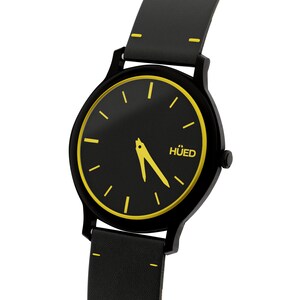 May include: A black wristwatch with a yellow rim around the face. The watch face is black with yellow hour markers and hands. The watch has a black leather strap with yellow stitching. The watch face has the word "H&Uuml;ED" printed on it.