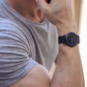 Puede incluir: Un reloj de pulsera negro con una esfera azul y una correa de cuero negra.