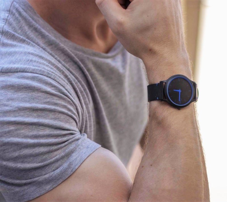 Puede incluir: Un reloj de pulsera negro con una esfera azul y una correa de cuero negra.