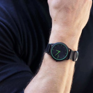Pode incluir: Um rel&oacute;gio de pulso preto com uma borda verde em torno do mostrador. O mostrador do rel&oacute;gio tem ponteiros brancos e um fundo preto com a palavra "KICCO" impressa em branco.