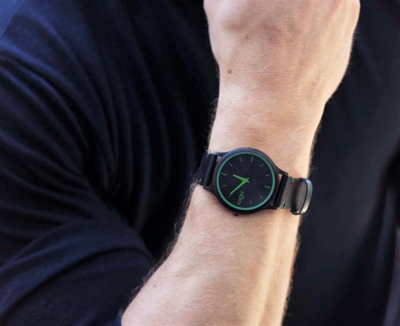 Pode incluir: Um rel&oacute;gio de pulso preto com uma borda verde em torno do mostrador. O mostrador do rel&oacute;gio tem ponteiros brancos e um fundo preto com a palavra "KICCO" impressa em branco.