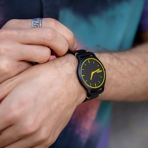 May include: A black wristwatch with a yellow face and black hands. The watch has a black strap and the word "HUGO" is printed on the face.
