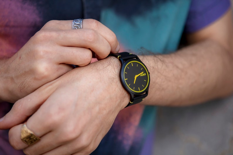 May include: A black wristwatch with a yellow face and black hands. The watch has a black strap and the word "HUGO" is printed on the face.