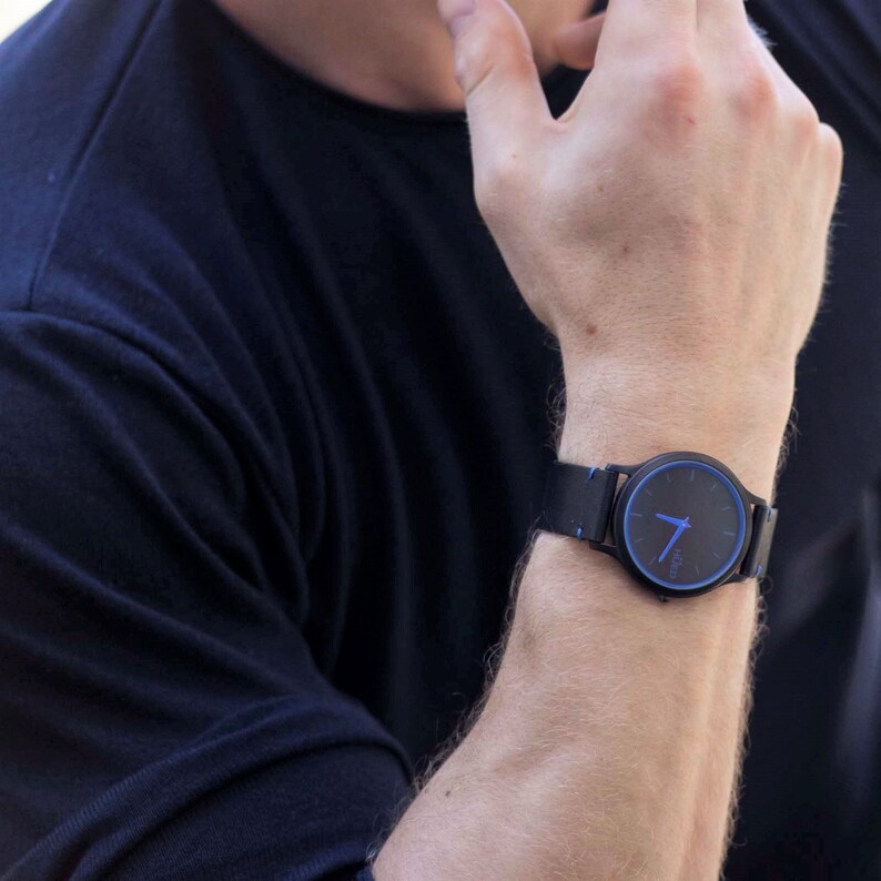Puede incluir: Un reloj de pulsera negro con una esfera azul y una correa de cuero negro. El reloj tiene un dise&ntilde;o sencillo con manecillas blancas y marcadores de hora.
