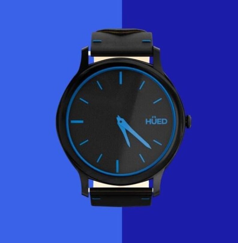 Puede incluir: Un reloj de pulsera negro con un borde azul alrededor de la esfera. La esfera del reloj es negra con agujas de hora y minuto azules y la palabra "HUED" en letras blancas. El reloj tiene una correa negra.