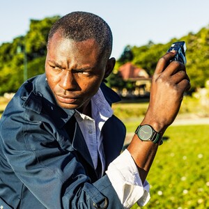 Pode incluir: Um homem vestindo uma jaqueta azul e uma camisa branca com um rel&oacute;gio verde no pulso, segurando uma c&acirc;mera na m&atilde;o direita.