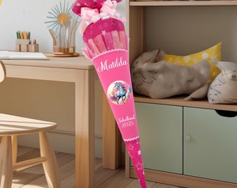 May include: Pink school cone with a unicorn design and the name Matilda. The cone has white stars and the text "Schulkind 2023".