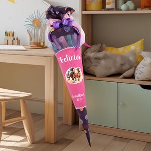 Könnte beinhalten: Ein rosa-lilafarbener Schultüte mit einem Pferde-Motiv und dem Namen "Felicia" darauf gedruckt. Die Tüte ist mit lila-schwarzen Punkten und dem Text "Schulkind 2023" verziert.