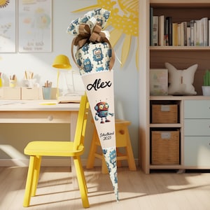 Op de afbeelding: Een beige en bruine schoolkegel met een robotpatroon. De kegel heeft een wit lint en een label met de naam "Alex" en de tekst "Schulkind 2023".