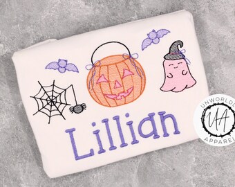 Może przedstawiać: Biały prostokątny przedmiot z haftem o tematyce Halloween. Zawiera dynię, ducha, nietoperze, pajęczynę i imię "Lillian" w kolorze fioletowym. Zawiera okrągłe logo z napisem "Unworldly Apparel".