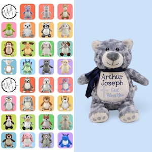 May include: A gray plush bear with a dark blue ribbon tied around its neck. The bear features an embroidered white patch on its chest displaying the name Arthur Joseph, a cross symbol, and the text God Bless You in dark blue embroidery.