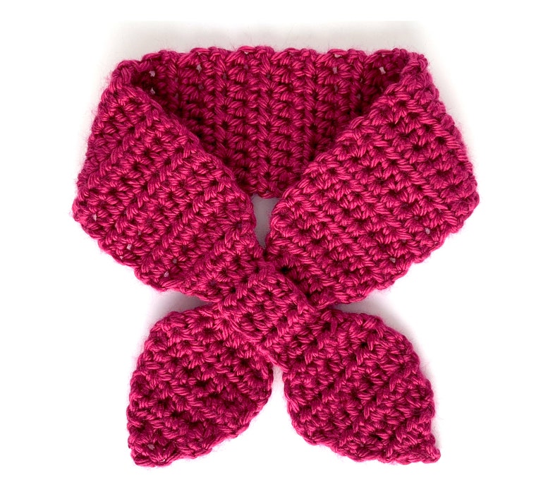 May include: A pink crocheted neck scarf with a bow tie design.