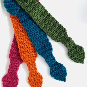 May include: Four crocheted tie-like fabric strips in different colors: teal, orange, green, and pink. The strips are arranged in a fan shape with the tips pointing to the right.