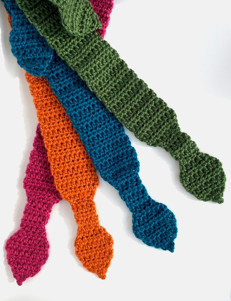 May include: Four crocheted tie-like fabric strips in different colors: teal, orange, green, and pink. The strips are arranged in a fan shape with the tips pointing to the right.