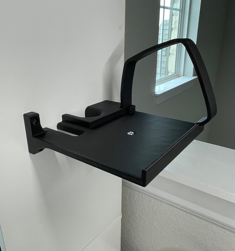 Puede incluir: Estante de pared negro con un brazo curvo para sujetar un dispositivo. El estante est&aacute; hecho de pl&aacute;stico y tiene un acabado mate.