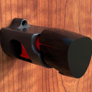 May include: A black plastic wall mount with a red accent, designed to hold a cylindrical object. The mount has a rounded, slightly angled end.