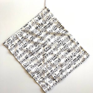 May include: A white fabric bag with black musical notes printed on it. The bag has two white drawstrings.