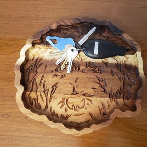 May include: A wooden tray carved in the shape of a dog's head. The tray is brown and has a natural wood finish. There are keys and a car key fob in the tray.