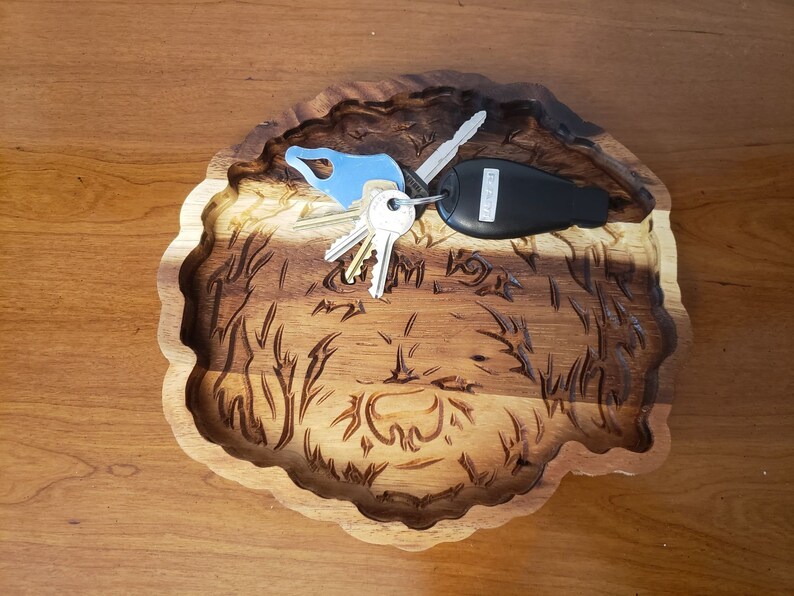 May include: A wooden tray carved in the shape of a dog's head. The tray is brown and has a natural wood finish. There are keys and a car key fob in the tray.