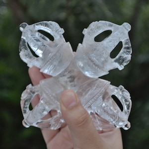 May include: A clear quartz crystal sculpture of a vajra, a ritual weapon in Buddhism, with intricate details. The vajra is a symbol of strength, power, and enlightenment.