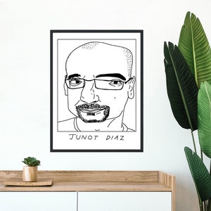Puede incluir: Impresión artística enmarcada en negro con un retrato en blanco y negro de un hombre con gafas. El texto "JUNOT DIAZ" está impreso en negro en la parte inferior de la imagen. La obra de arte se muestra en una pared blanca.