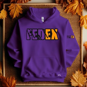 Op de afbeelding: Een paarse hoodie met een voorzak. Het woord "FEDEX" is in zwarte en oranje blokletters op de borst gedrukt. Een kleinere versie van het logo staat op de rechter mouw.