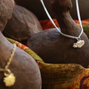 May include: A silver chain necklace with a cloud-shaped pendant. The necklace is displayed on a brown wooden surface with a colorful fabric background.