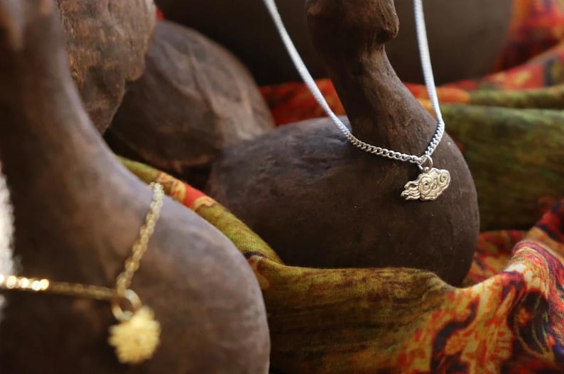 May include: A silver chain necklace with a cloud-shaped pendant. The necklace is displayed on a brown wooden surface with a colorful fabric background.