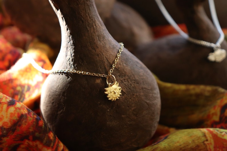 May include: A gold necklace with a sun pendant hangs on a dark brown gourd. The gourd is sitting on a colorful fabric.