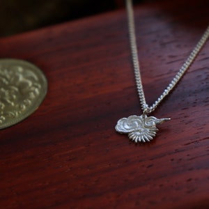 Op de afbeelding: Een zilveren ketting met een wolkvormige hanger. De hanger is gedetailleerd met een draaiend ontwerp en een kleine zon.