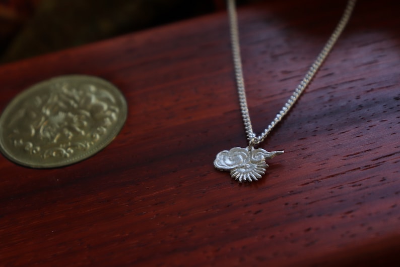 Op de afbeelding: Een zilveren ketting met een wolkvormige hanger. De hanger is gedetailleerd met een draaiend ontwerp en een kleine zon.