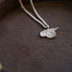 Op de afbeelding: Een zilveren ketting met een delicate ketting en een hanger in de vorm van een gestileerde bloem met een swirl-ontwerp.