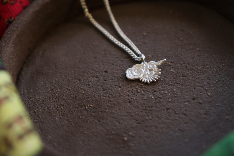 Op de afbeelding: Een zilveren ketting met een delicate ketting en een hanger in de vorm van een gestileerde bloem met een swirl-ontwerp.