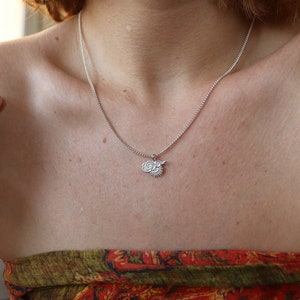 Op de afbeelding: Een zilveren ketting met een klein hanger met een gestileerd zon- en wolkmotief.