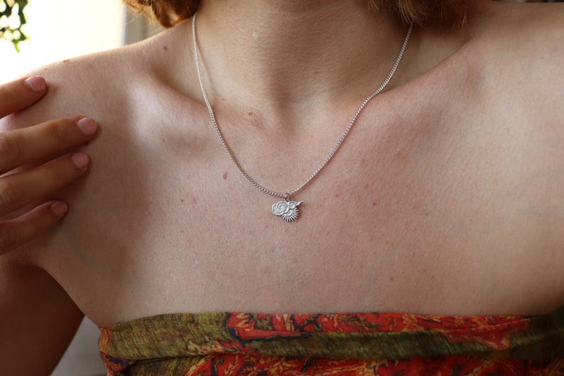 Op de afbeelding: Een zilveren ketting met een klein hanger met een gestileerd zon- en wolkmotief.