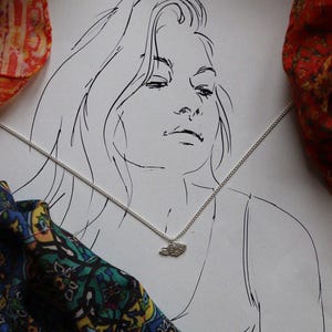 May include: A line drawing of a woman with long hair wearing a silver chain necklace with a small cloud pendant.