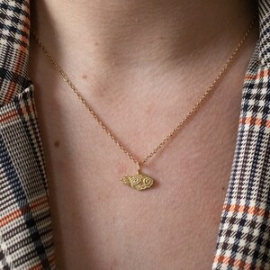 May include: A gold chain necklace with a small, detailed cloud pendant. The necklace is worn by a person wearing a plaid shirt.