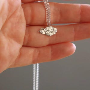 May include: A silver chain necklace with a small, detailed cloud pendant.