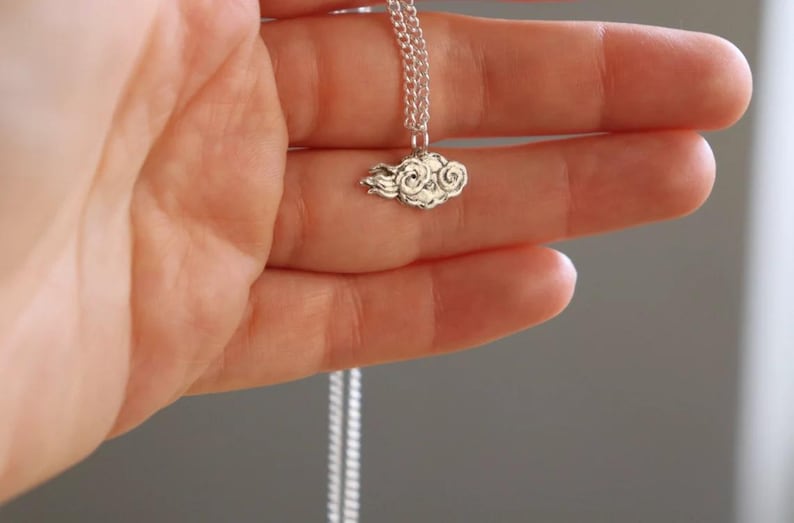 May include: A silver chain necklace with a small, detailed cloud pendant.