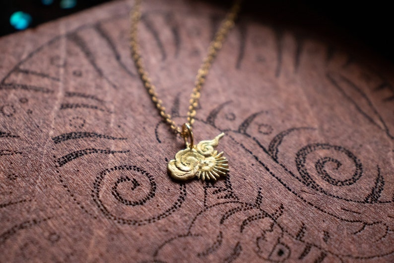 Op de afbeelding: Een gouden ketting met een hanger in de vorm van een zon en wolken. De hanger is gedetailleerd met draaiende lijnen en een zonnestralenontwerp.