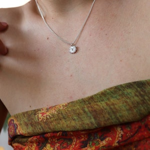 May include: A silver chain necklace with a small, silver sun pendant. The necklace is worn by a person with fair skin.